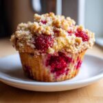 A single, perfectly baked Raspberry Streusel Muffin topped with golden brown streusel sits on a small white plate.