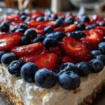Close-up of a rich Red, White & Blue Cheesecake Dip topped generously with fresh blueberries and sliced strawberries.