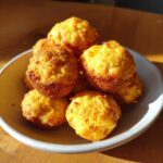 A pile of golden brown Southern-Style Cornbread Poppers stacked in a light-colored bowl.