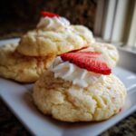 Close-up of three Strawberry Shortcake Butter Cookies stacked, topped with whipped cream and a fresh strawberry slice.