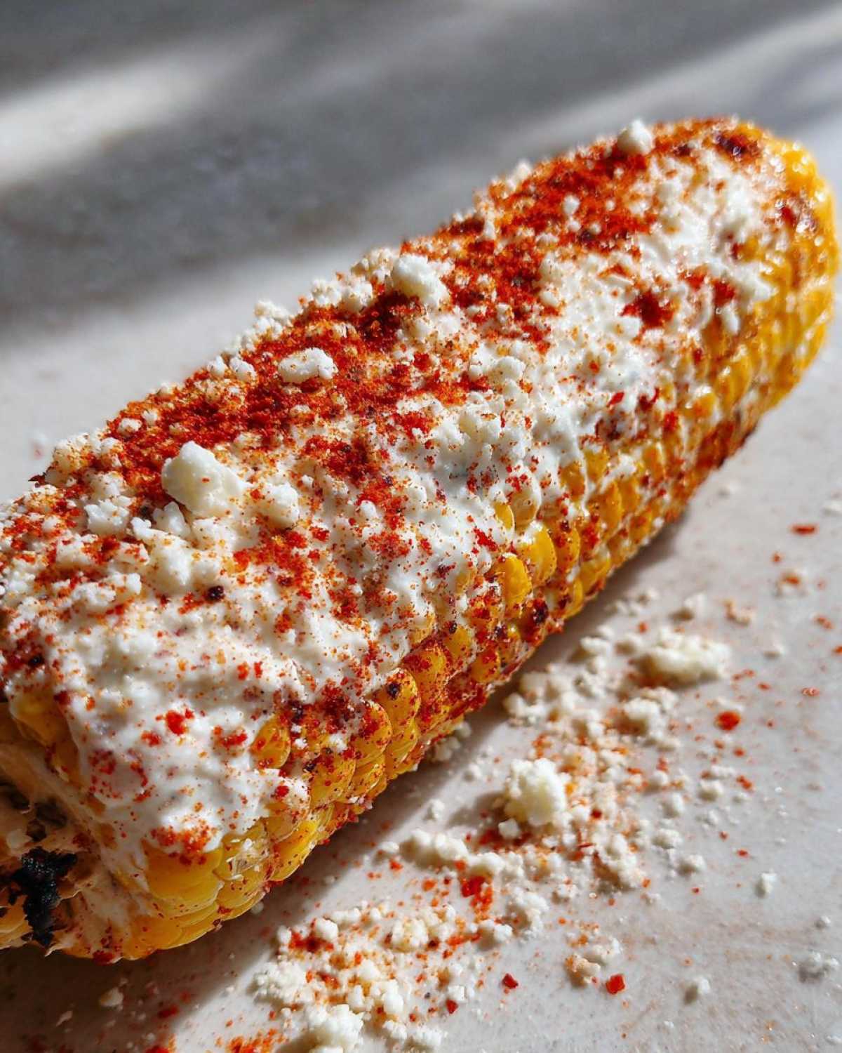 Close-up of grilled Street-Style Mexican Corn on the Cob covered in white cheese and red chili powder.